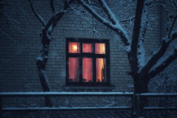 a dark house with a lit window to represent cozy horror